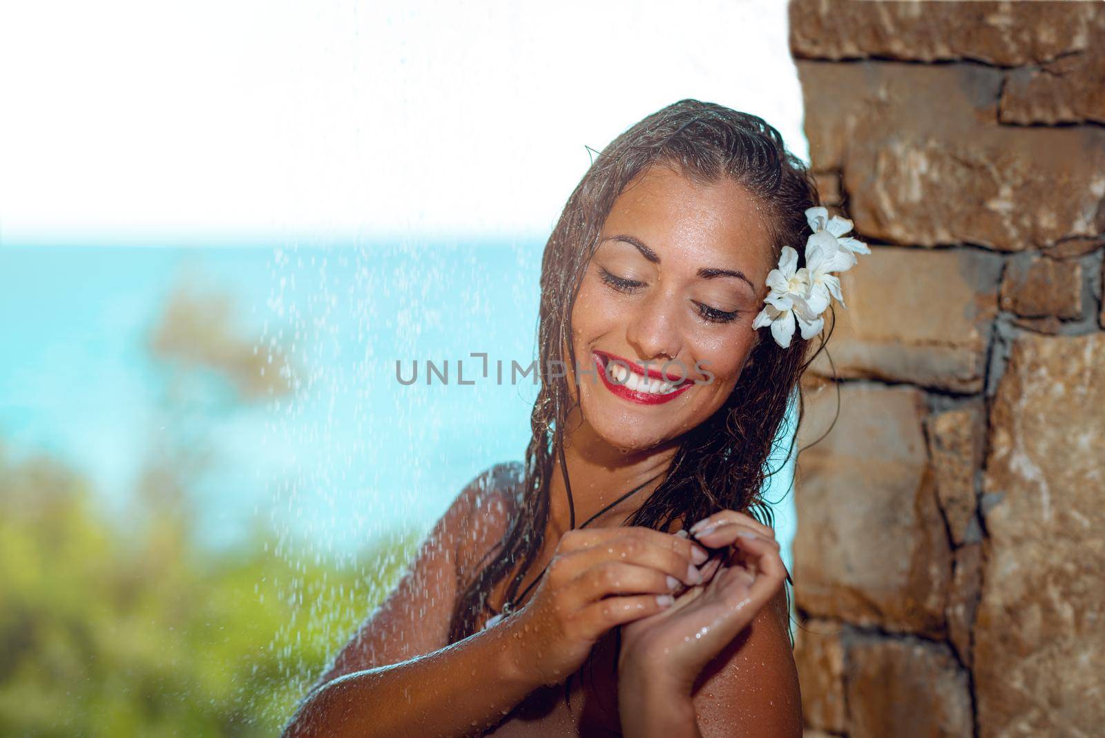 Beautiful young woman enjoying under a shower on the beach daydreaming about love.