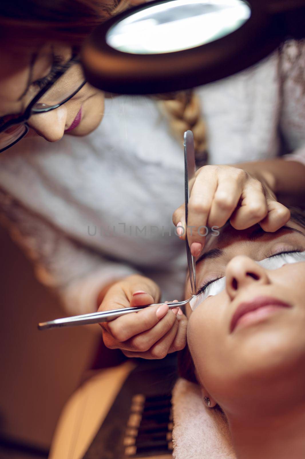 Beautician applying extended eyelashes to model at the beauty salon.