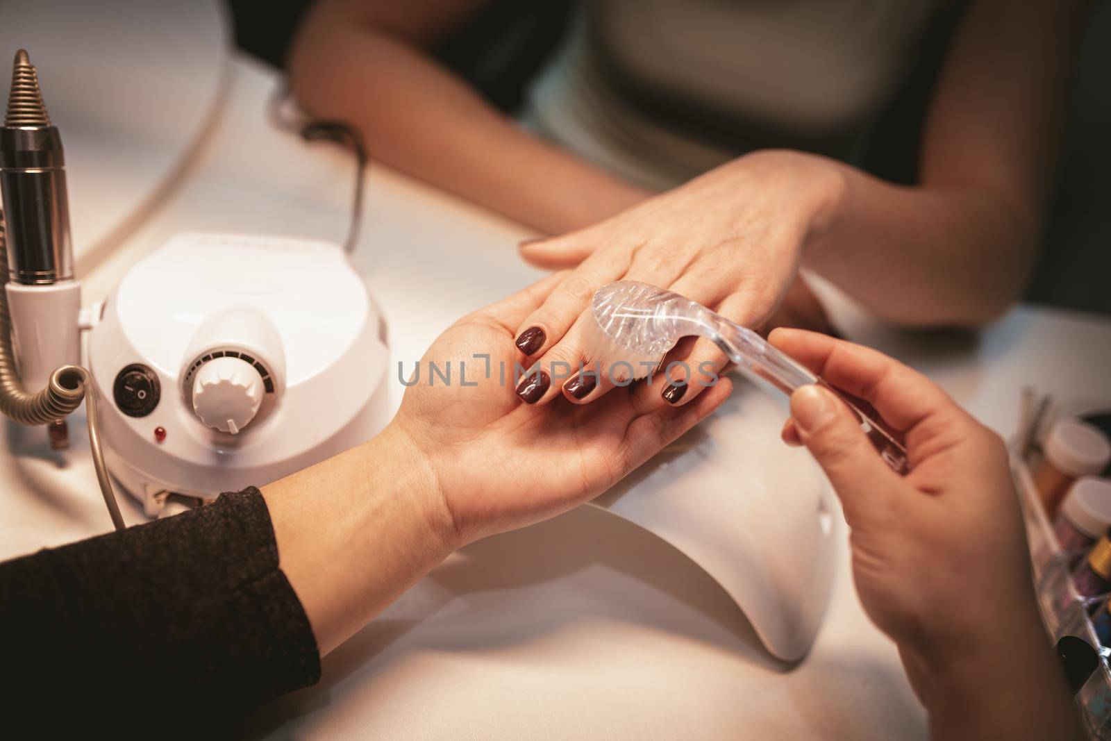 Close-up of a beautician hands brushing female clients nails after manicure process at the beauty salon.