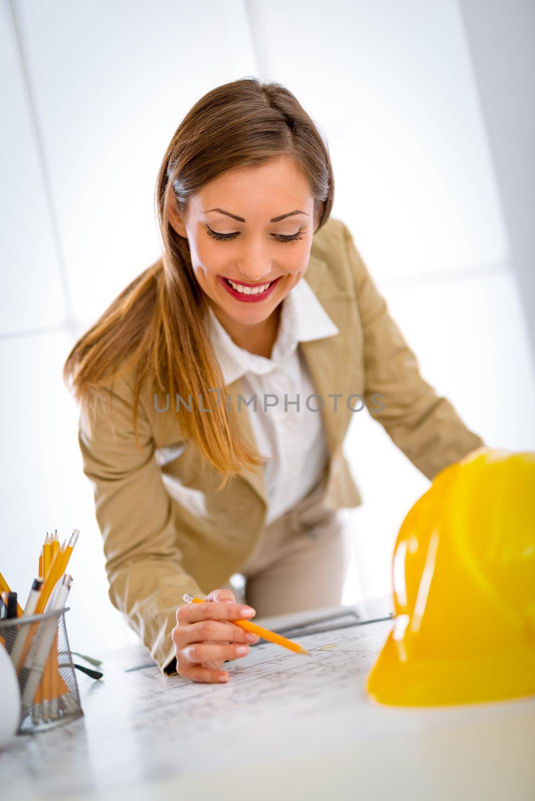 Smiling young woman architect constructor analyzing blueprint at desk in office. 