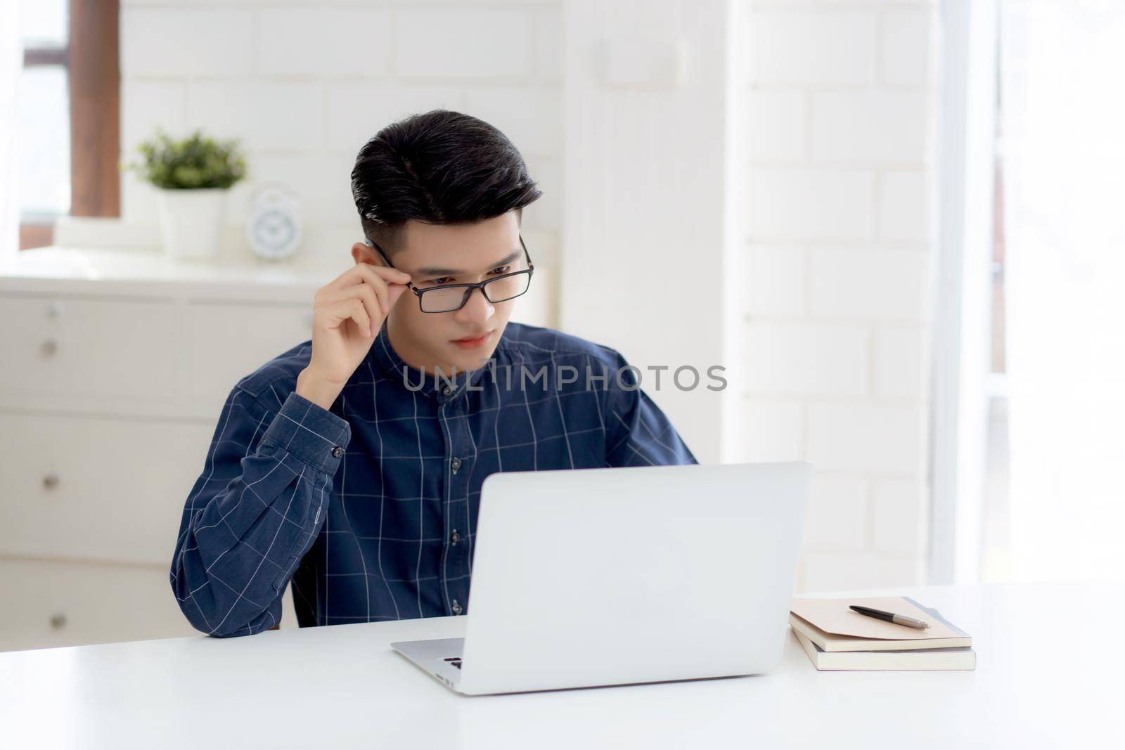 Young business man in glasses working from home with laptop computer on desk, freelance male sitting stay home using notebook for communication on table, entrepreneur in startup business, new normal.