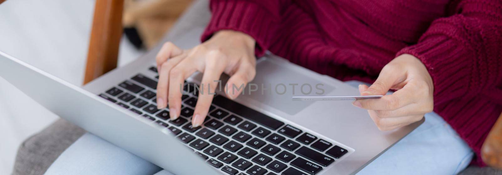 Closeup hand of young asian woman online shopping in Christmas with credit card on laptop computer, female buying and payment with debit card, xmas in holiday, happy new year, customer with purchase. by nnudoo