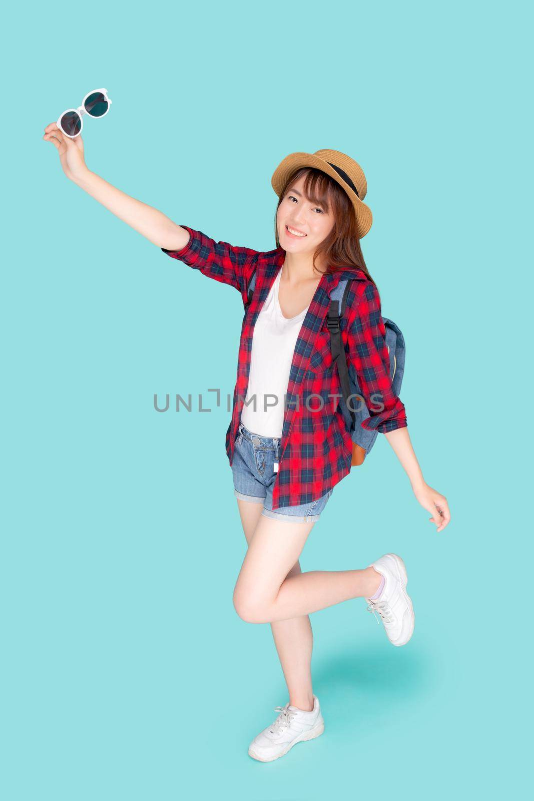 Beautiful portrait young asian woman wear hat and holding sunglasses smile expression confident enjoy summer holiday isolated blue background, model girl fashion having backpack, travel concept. by nnudoo