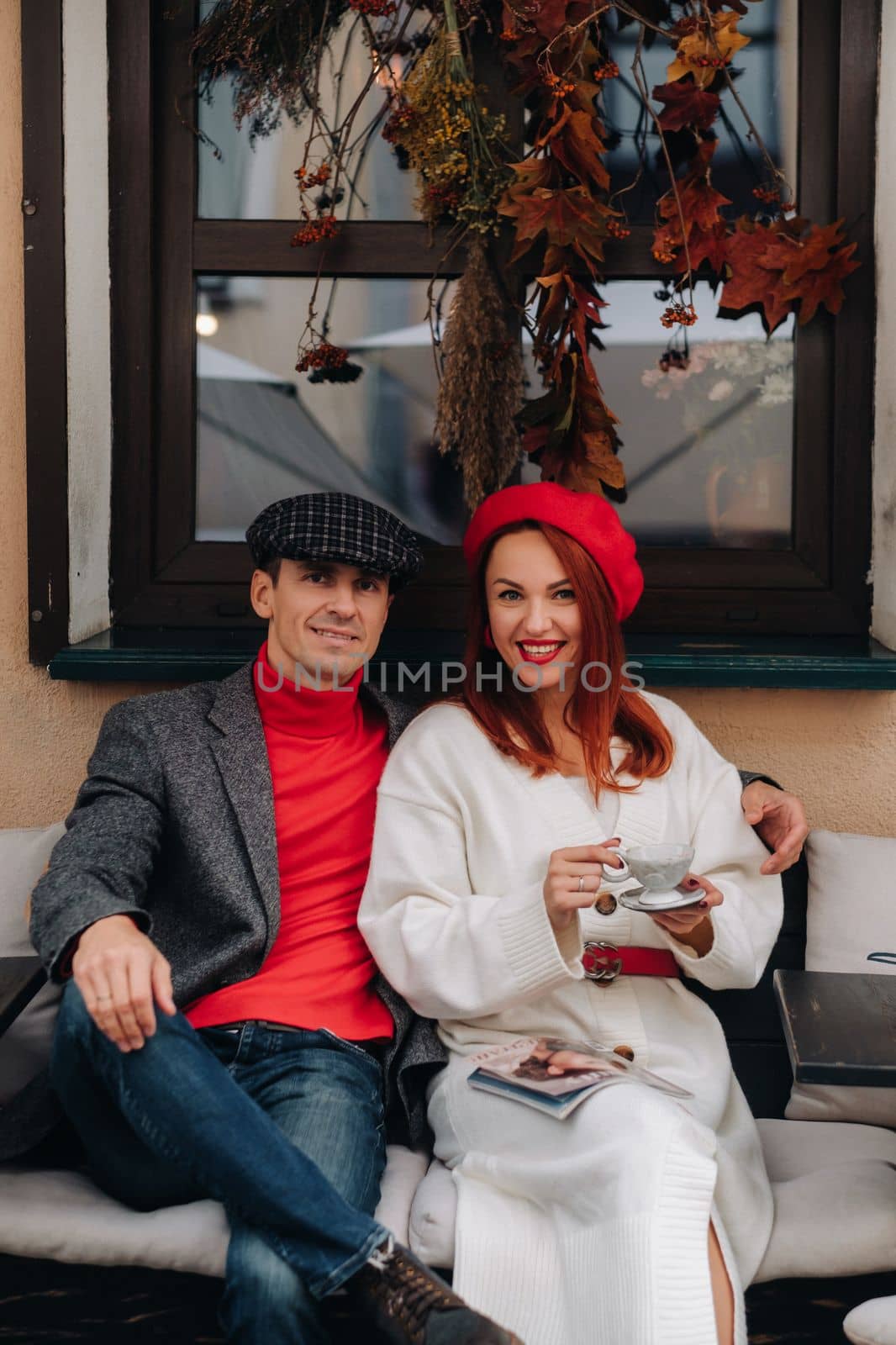 A happy stylish couple drinks coffee and smiles while sitting in a cafe on the street.