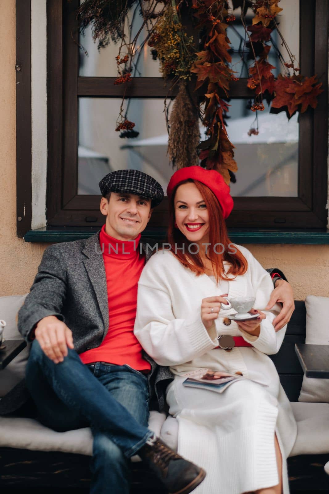 A happy stylish couple drinks coffee and smiles while sitting in a cafe on the street by Lobachad