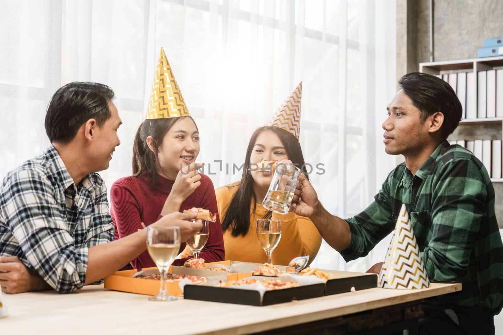 Group of diverse Asian friends gather to celebrate Christmas with champagne and eating pizza at home. Joy of holiday party with friends or colleague concept by nateemee