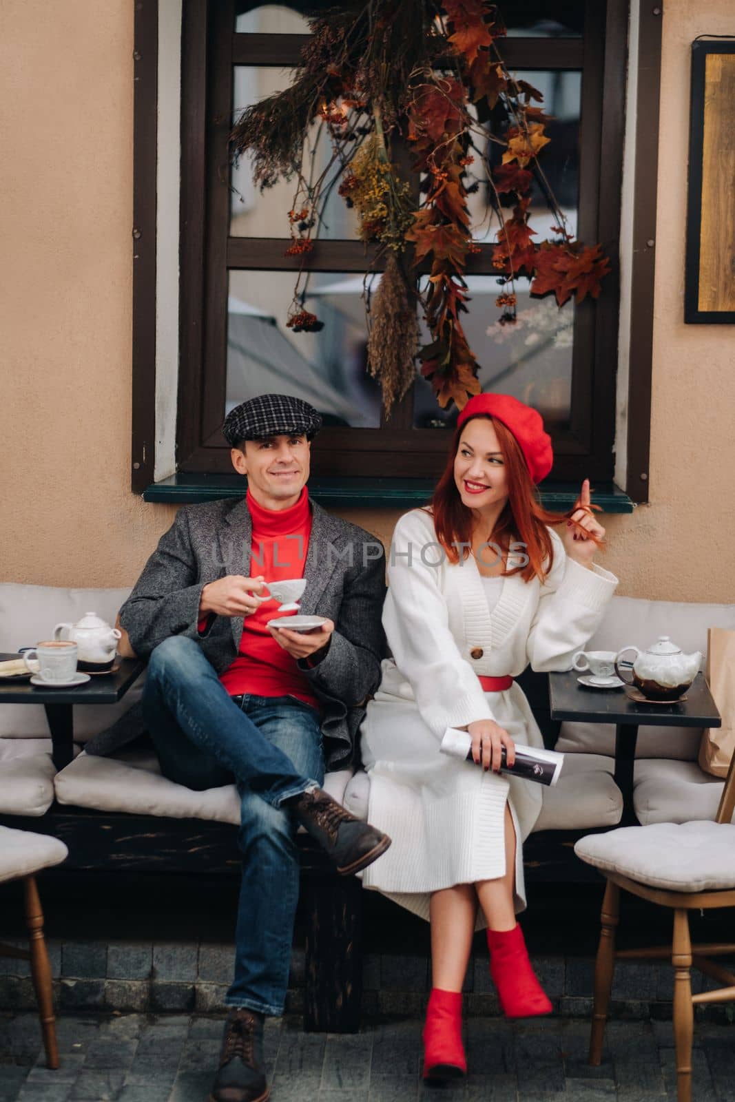 A happy stylish couple drinks coffee and smiles while sitting in a cafe on the street.