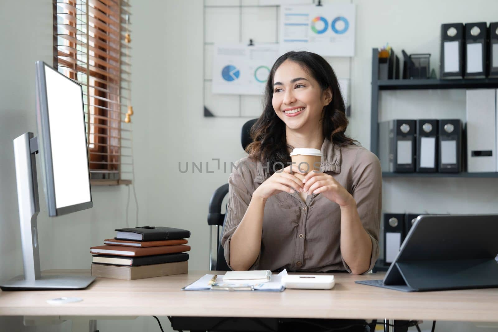 Beautiful young Asian businesswoman smiling holding a coffee mug and laptop working at the office..