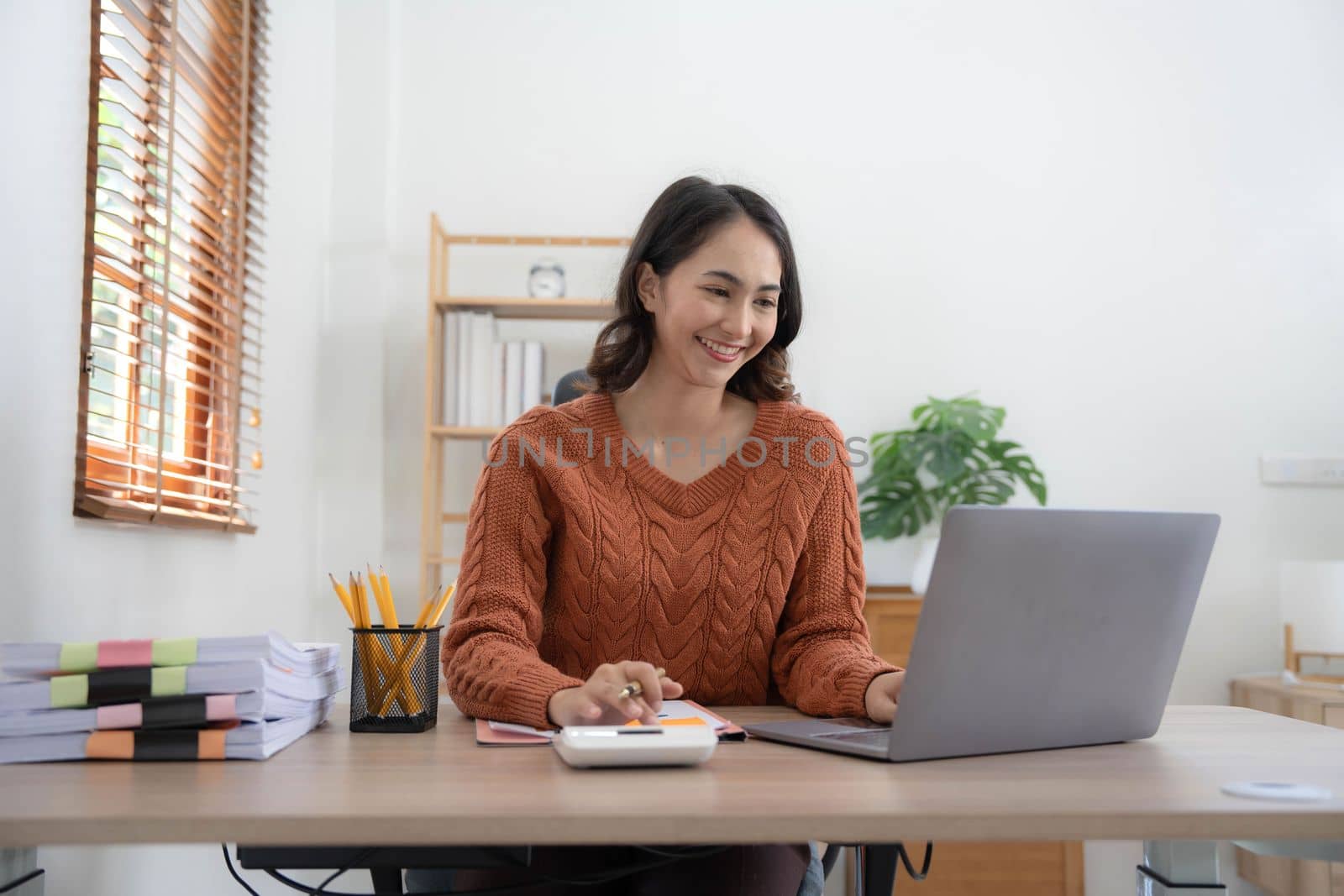 Asian indian Female director working in the office sitting at a desk analyzing business statistics holding diagrams and charts using a laptop computer,.