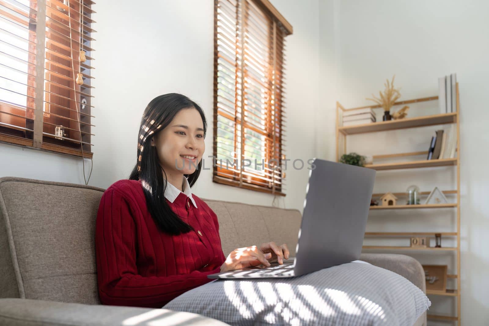 Young asian female using laptop computer and looking at the screen in living room, Remote Job or work from home concept