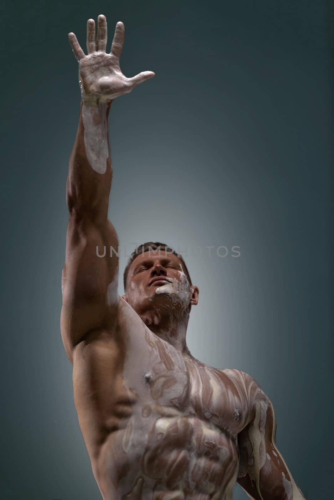 A muscular man with closed eyes motivatingly pulls his hand up with an open palm into the frame. An inspirational pose symbolizing aspiration