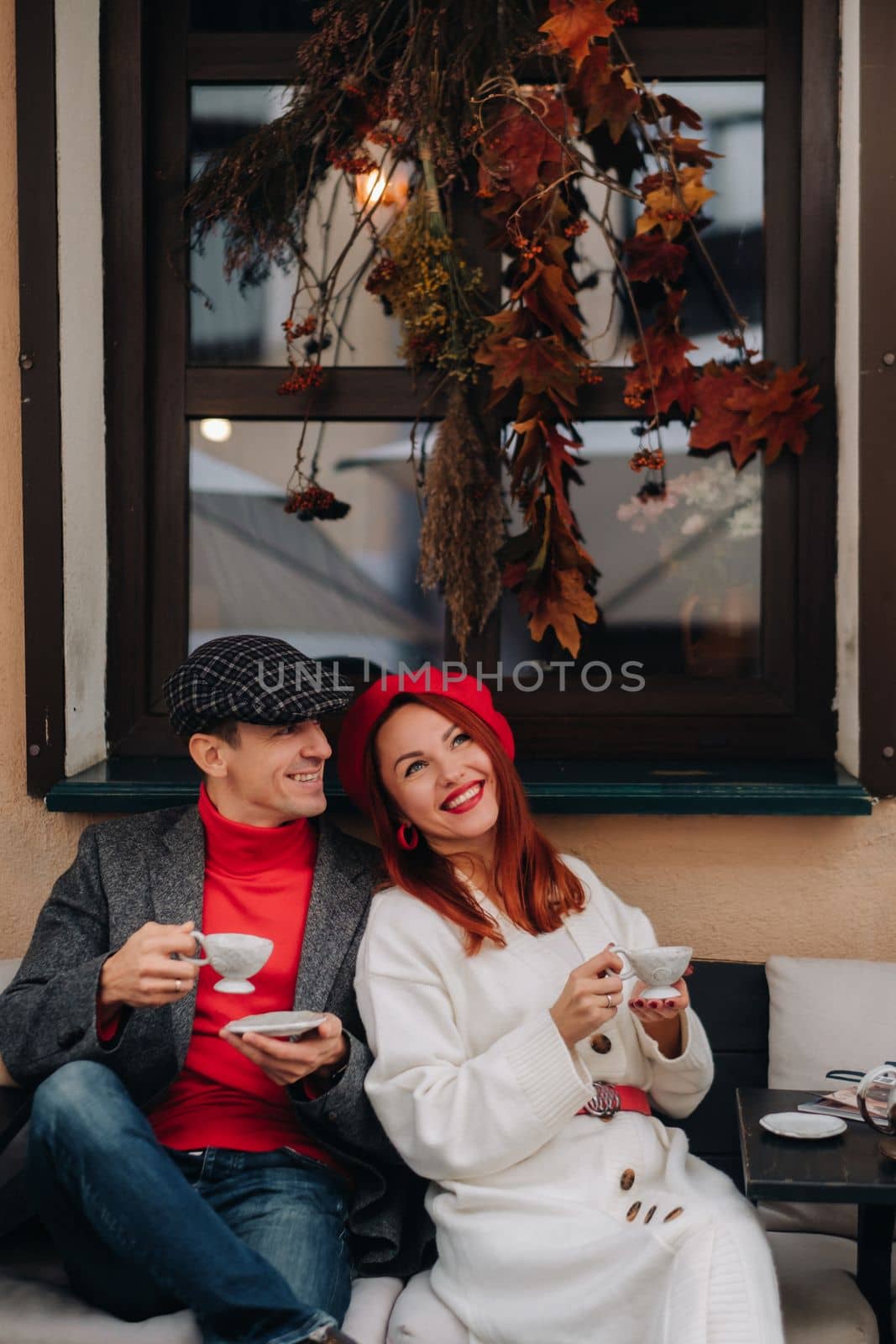 A happy stylish couple drinks coffee and smiles while sitting in a cafe on the street.