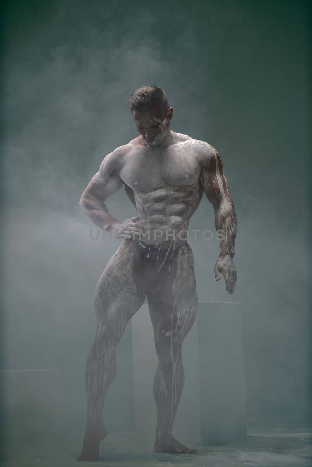 Studio shot of a muscular man. Young handsome athletic caucasian guy with beautiful naked torso looking down while posing shirtless isolated over grey background.