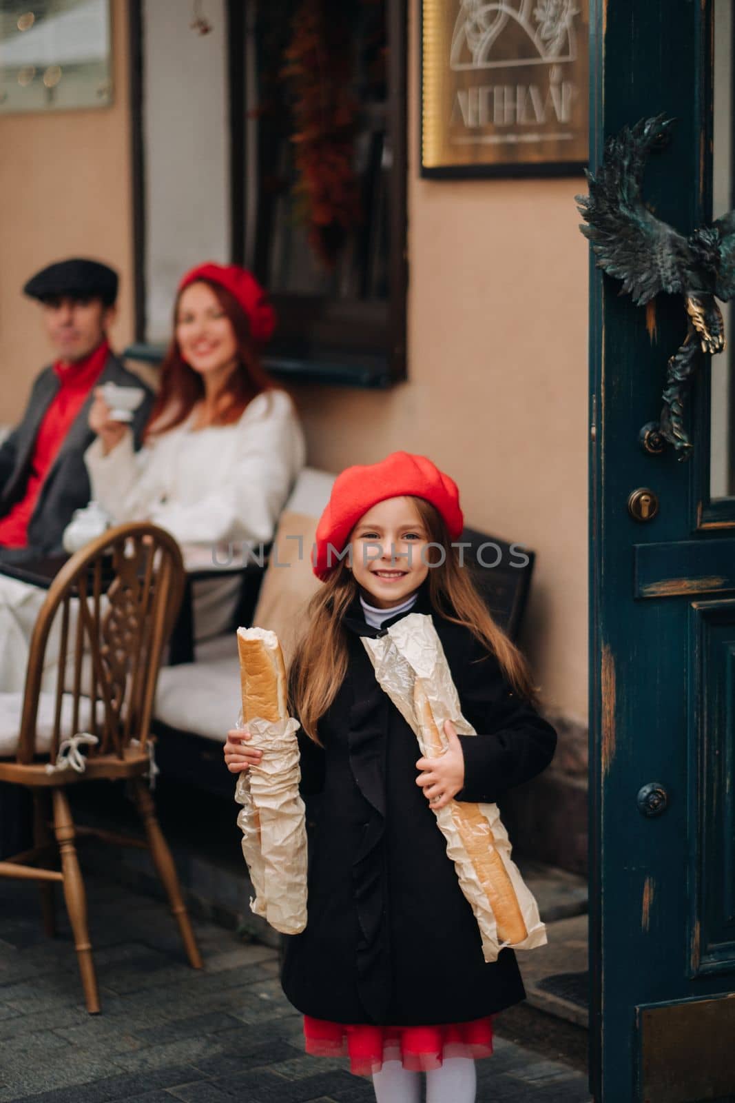 A stylish girl with baguettes stands near the store against the background of her parents.