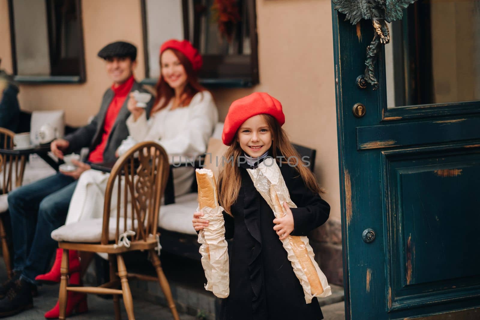 A stylish girl with baguettes stands near the store against the background of her parents.