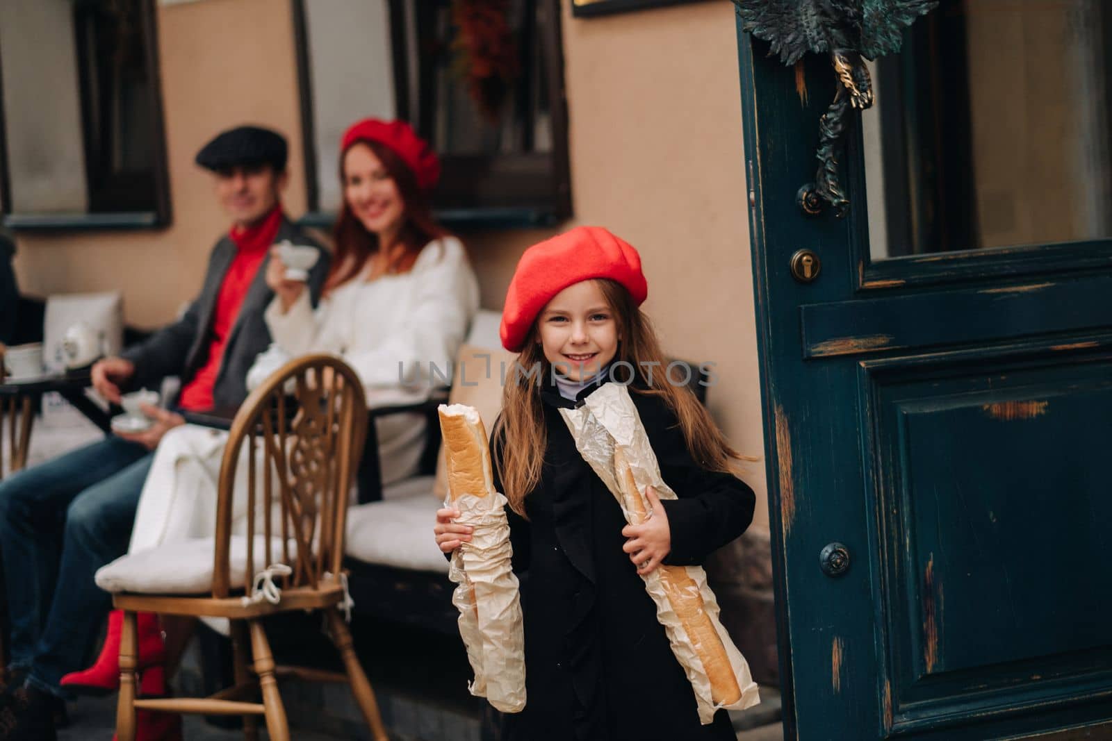 A stylish girl with baguettes stands near the store against the background of her parents.