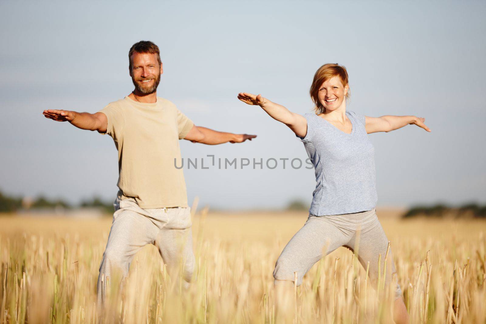 Yoga is part of their lifestyle. a mature couple in the warrior position during a yoga workout in a field. by YuriArcurs