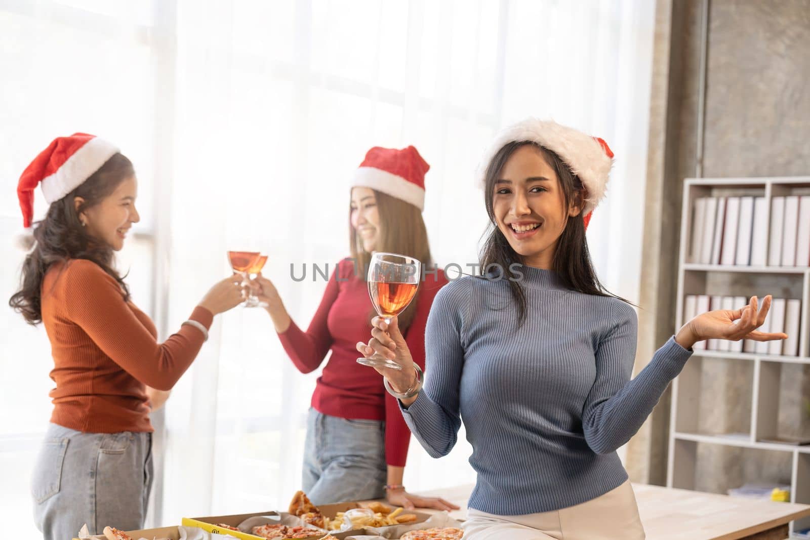 Group of Asian friends gather to celebrate Christmas with champagne and eating pizza at home. Joy of holiday party with friends or colleague concept.