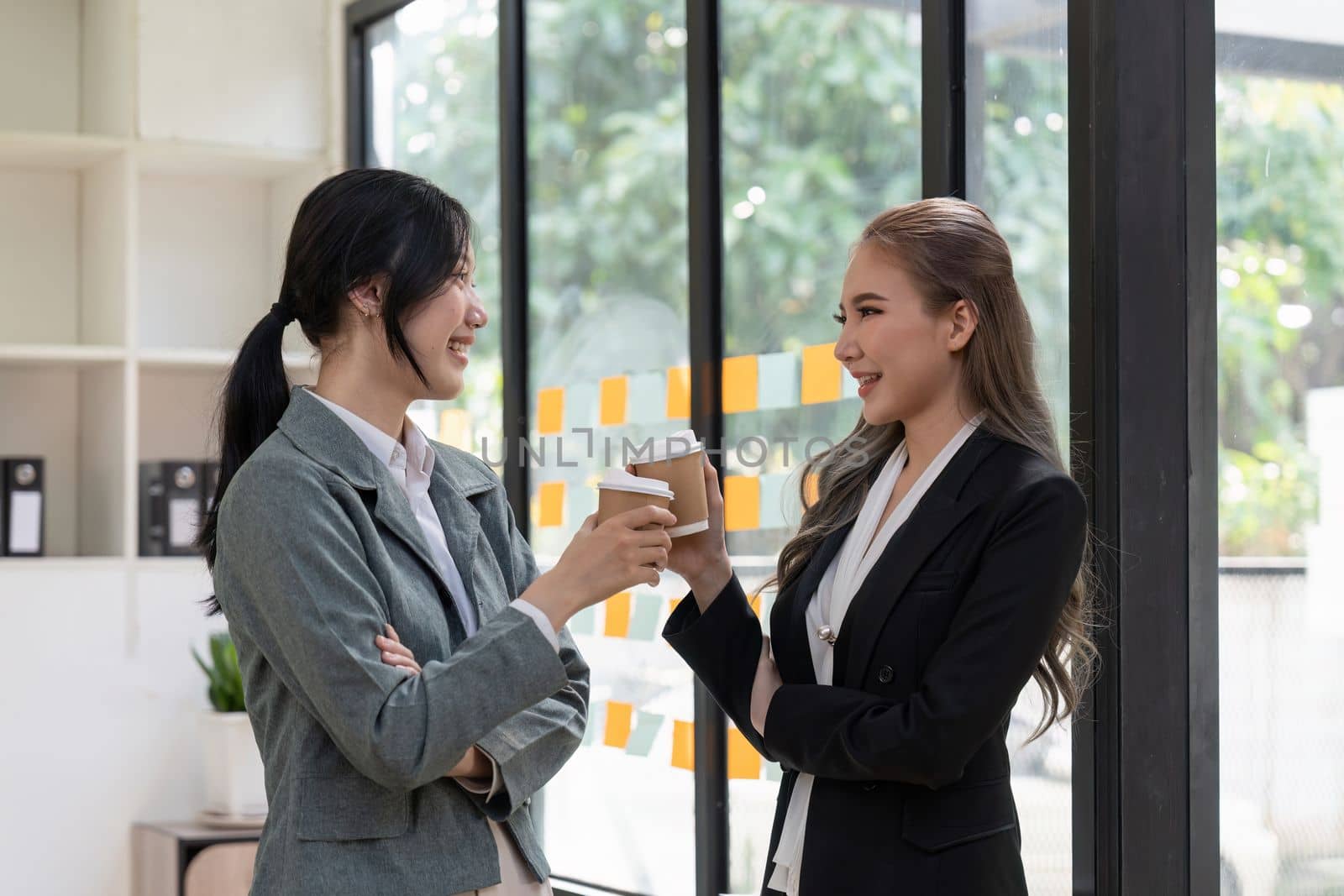 Diverse employees chatting during coffee break, walking in modern office, Asian businesswoman wearing glasses sharing ideas, discussing project with colleague, having pleasant conversation.