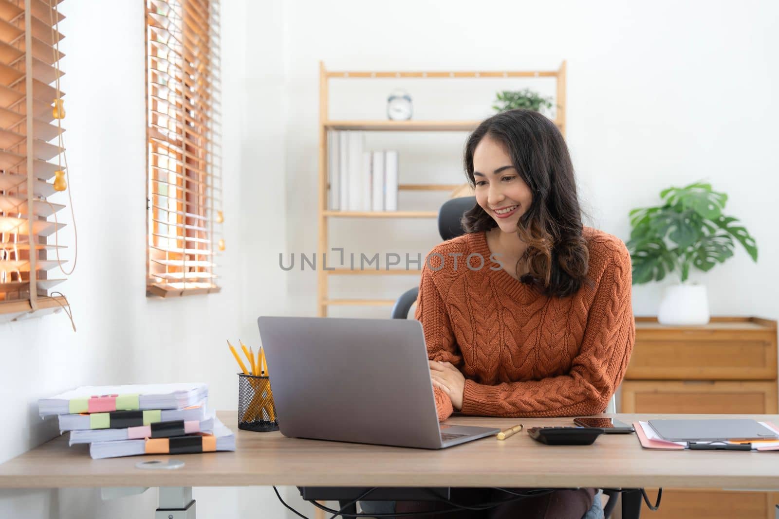 Focused Indian woman using laptop at home, looking at screen, chatting, reading or writing email, sitting on couch, serious female student doing homework, working on research project online.