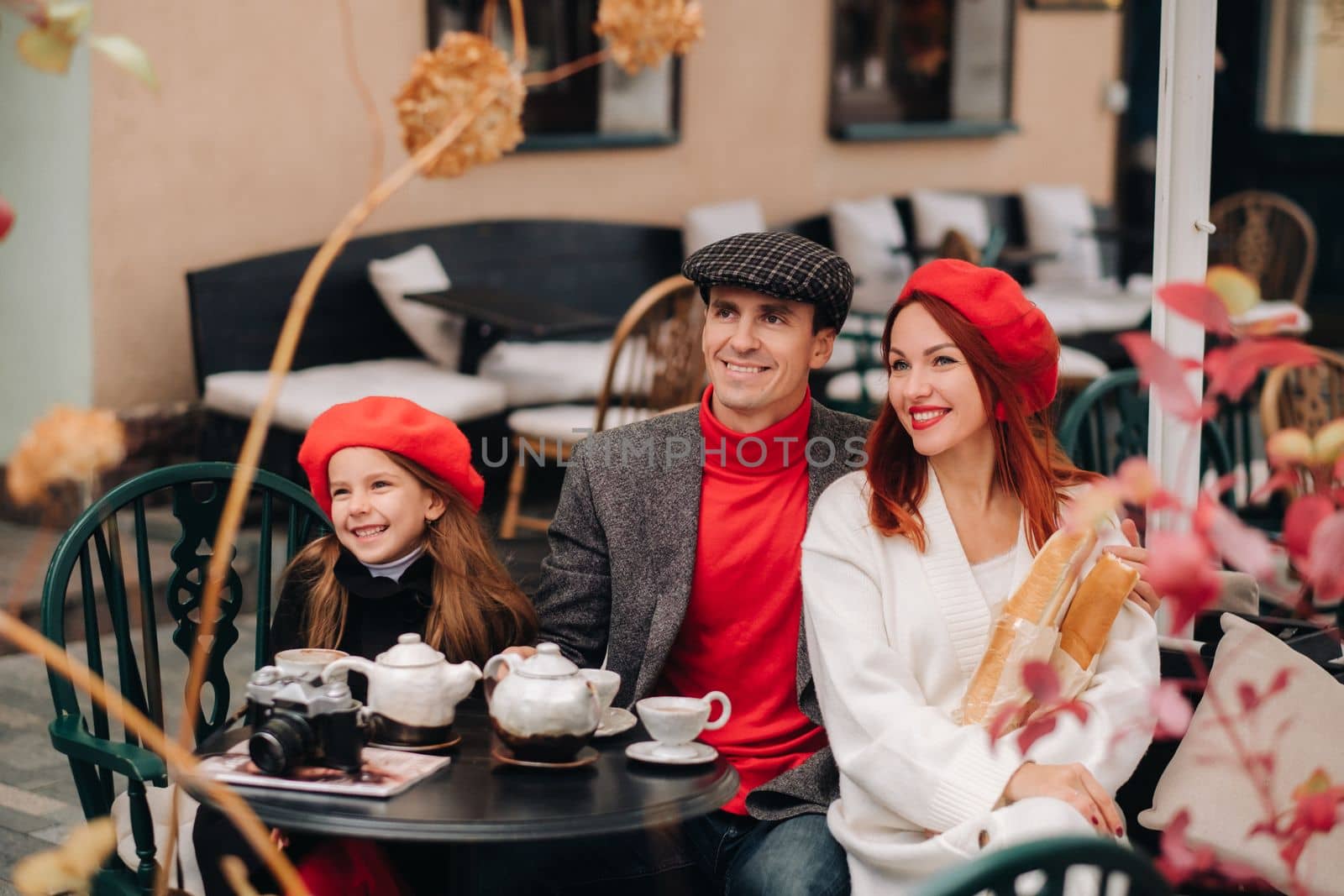 A stylish family gathered together in a cafe on the street. Mom, dad, little daughter drink tea, eat cakes. They are happy together. The concept of a happy family dinner.