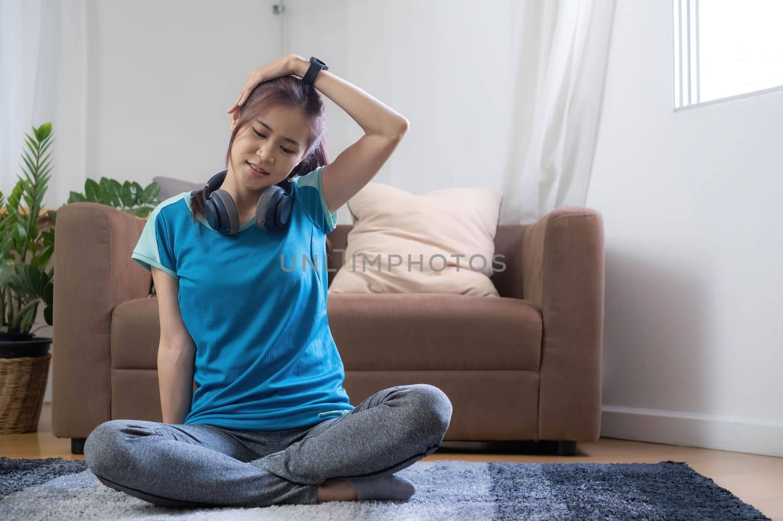Smiling Asian woman doing yoga shoulder stretching online class at home in living room. Self isolation and workout at home during COVID-19..