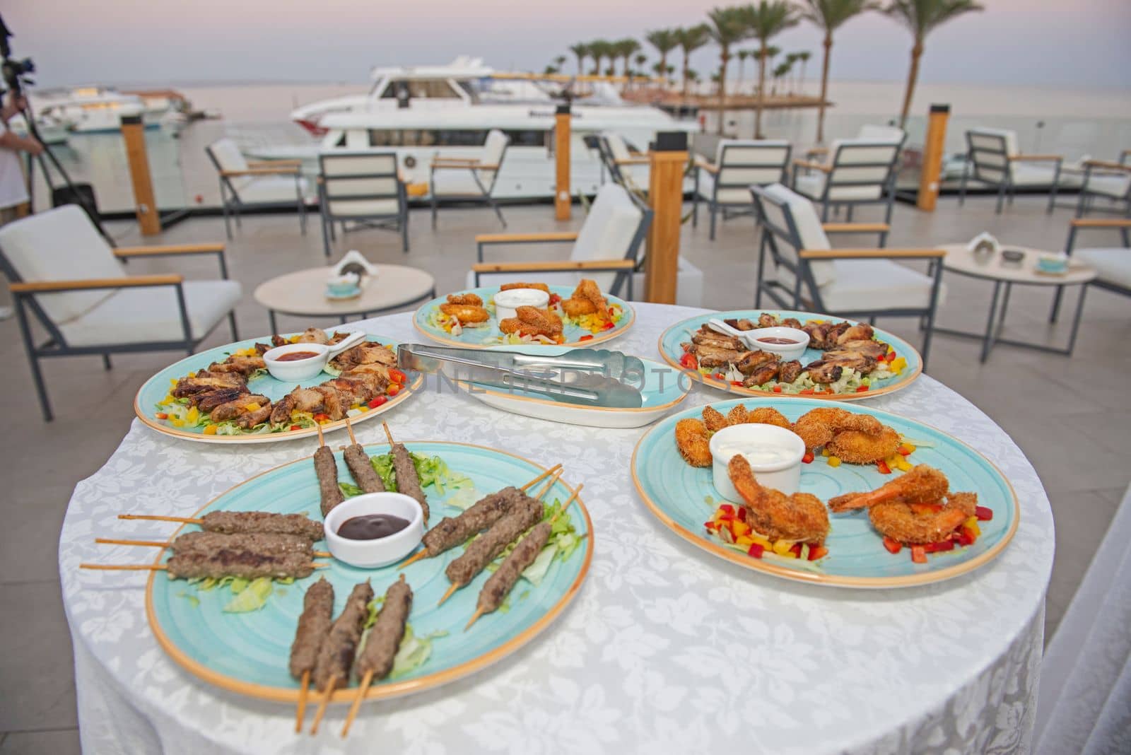 Selection display of meat dishes and finger food on a table at luxury outdoor restaurant buffet area with marina view