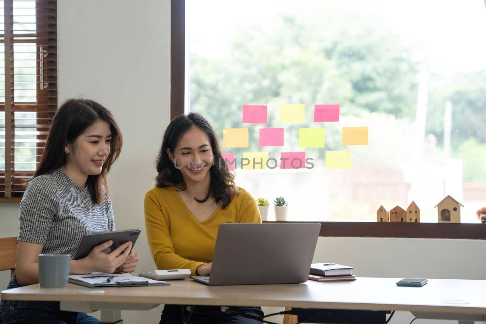 Two young Asian business woman talk, consult, discuss working with new startup project idea presentation analyze plan marketing and investment in the office. by wichayada