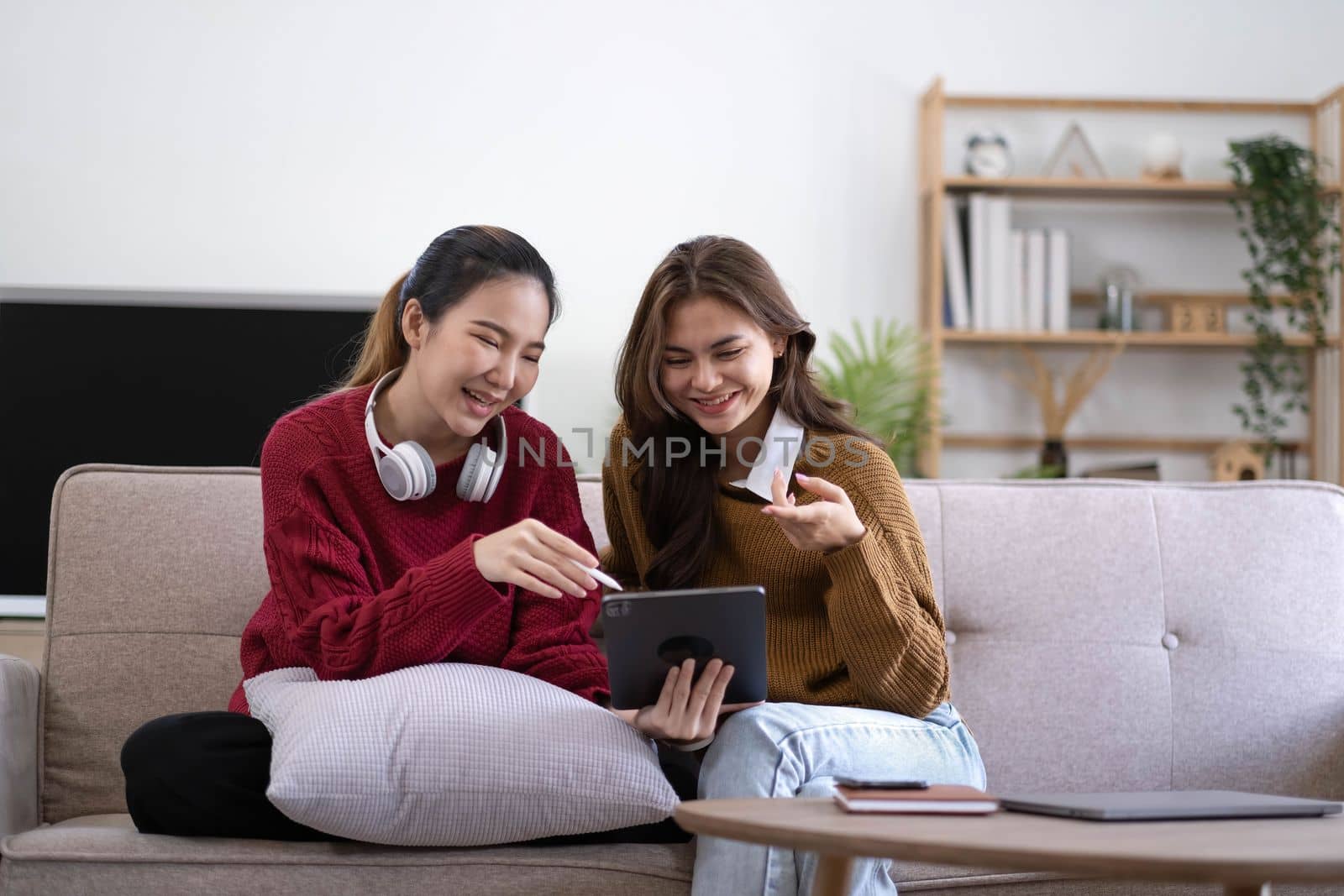 Two asian young woman happy smiling and using computer laptop on couch in living room at home.