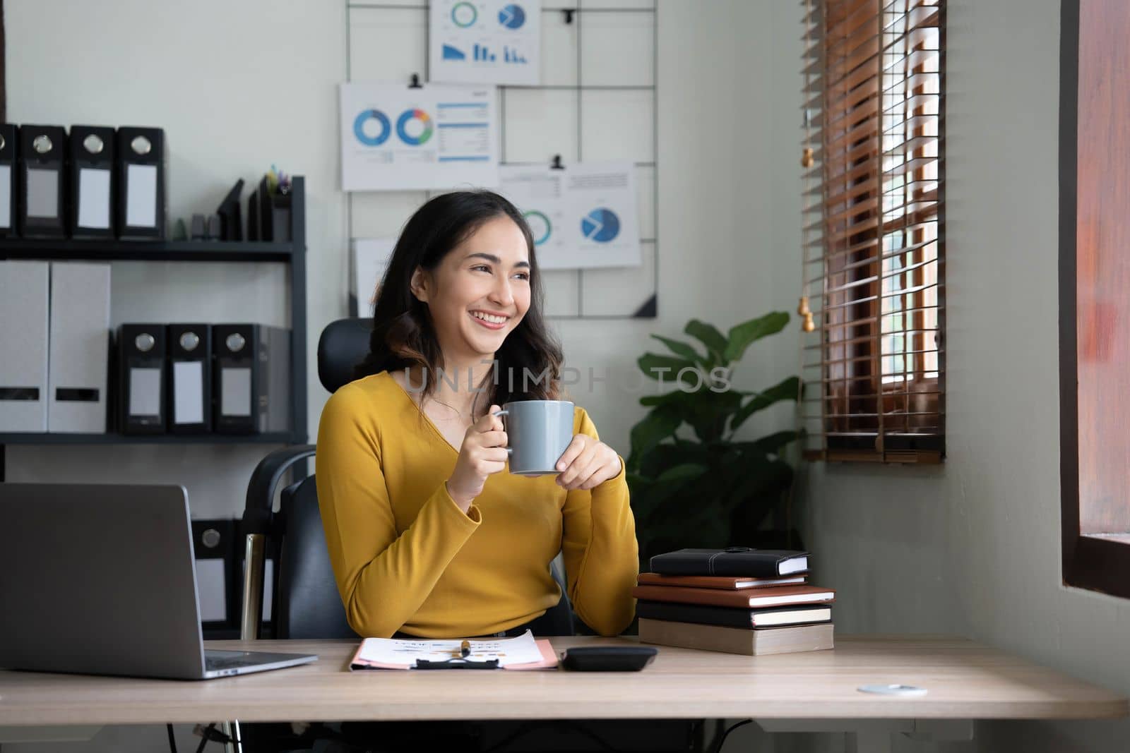 Beautiful young Asian businesswoman smiling holding a coffee mug and laptop working at the office..