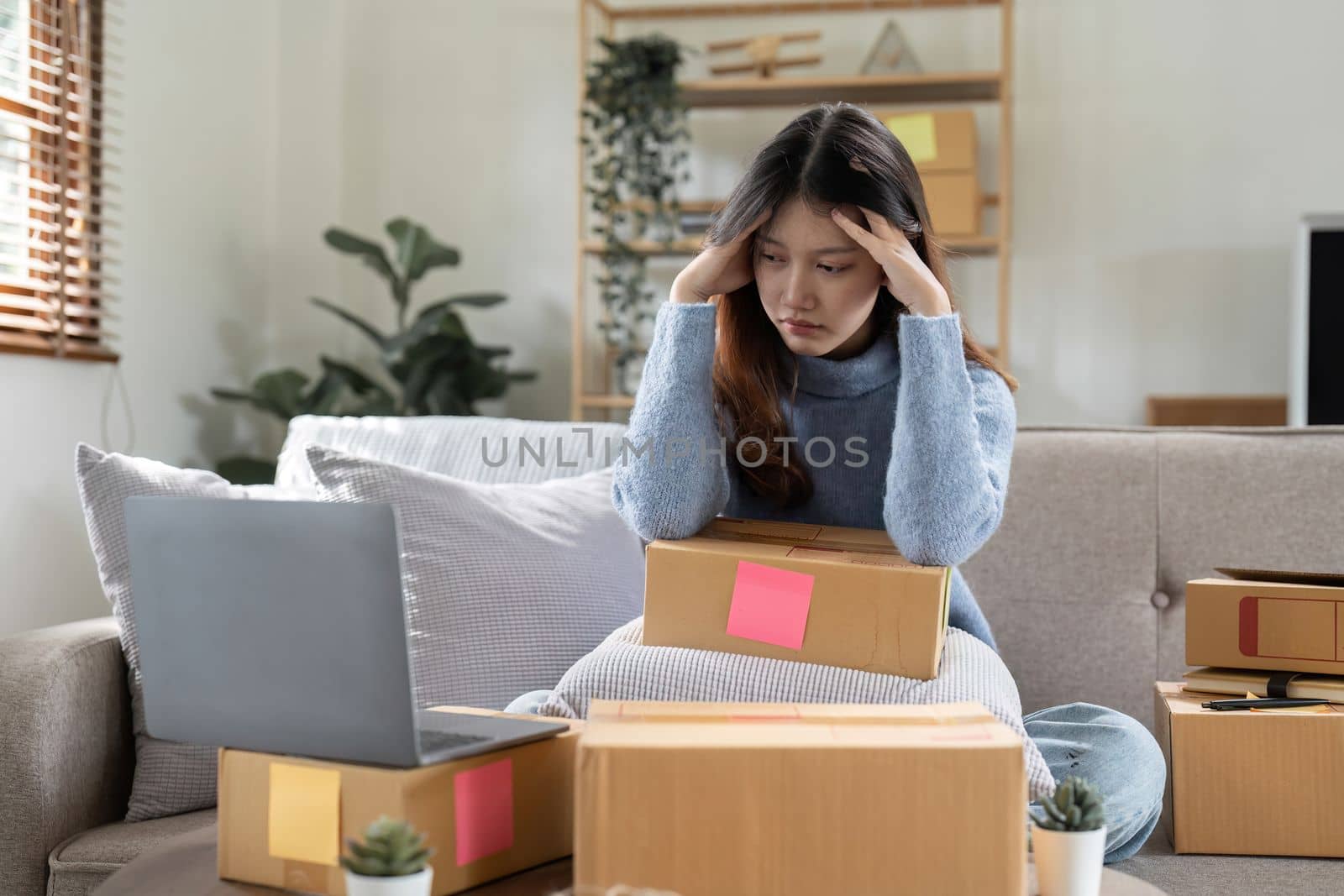 Stressed woman working with laptop computer and courier parcel box at home office. SME online ideas concept.