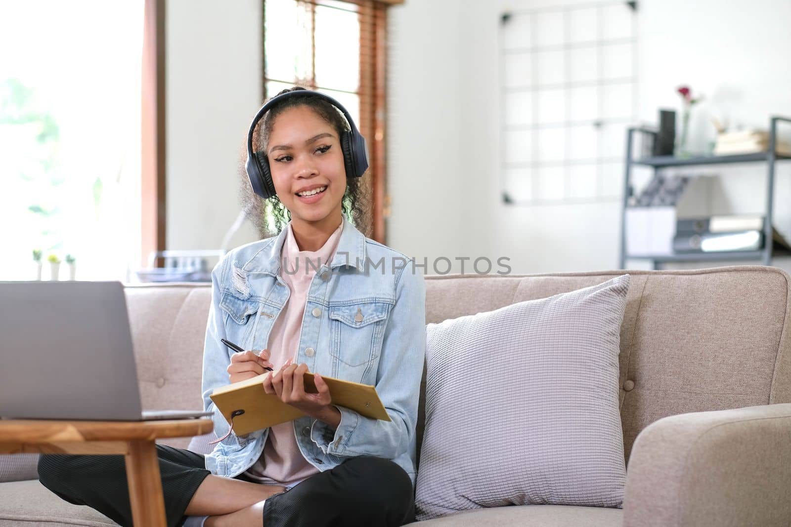Smiling Asian young female using headphones looking at laptop screen listen and learning online courses