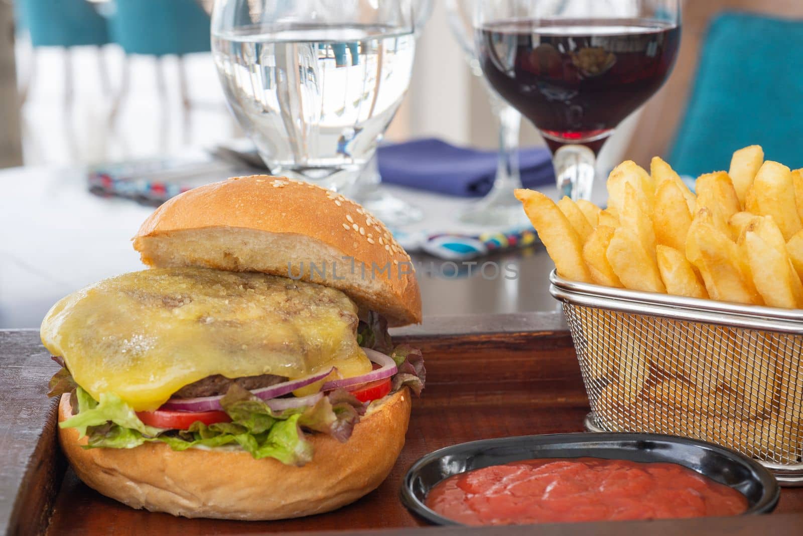 Cheeseburger a la carte meal with tomato sauce on wooden plate with dish of french fries chips
