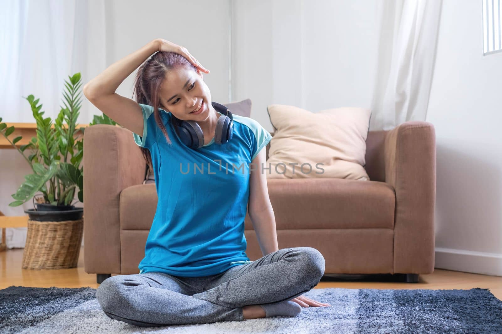 Smiling Asian woman doing yoga shoulder stretching online class at home in living room. Self isolation and workout at home during COVID-19..