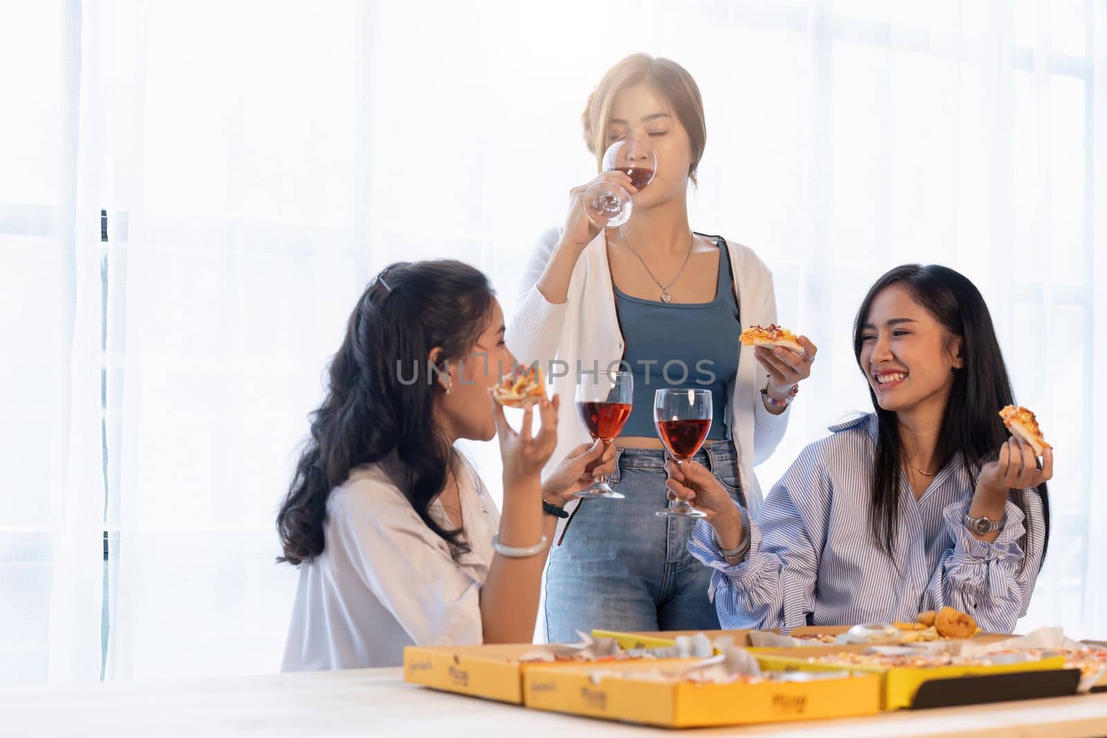 Group of Asian friends gather to celebrate Christmas with champagne and eating pizza at home. Joy of holiday party with friends or colleague concept.