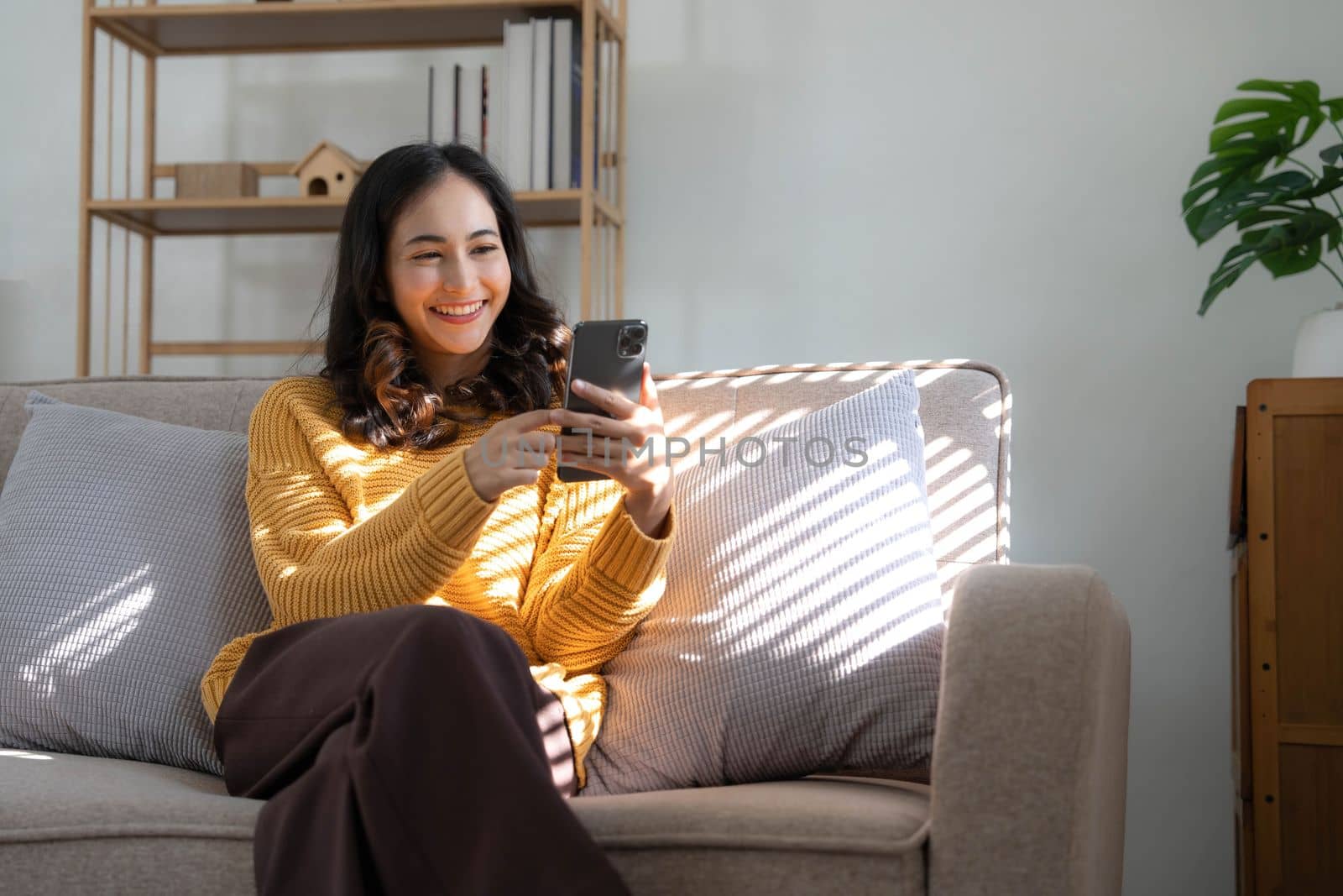 Happy girl checking social media holding smartphone at home. Smiling young latin woman using mobile phone app playing game, shopping online, ordering delivery relax on sofa..