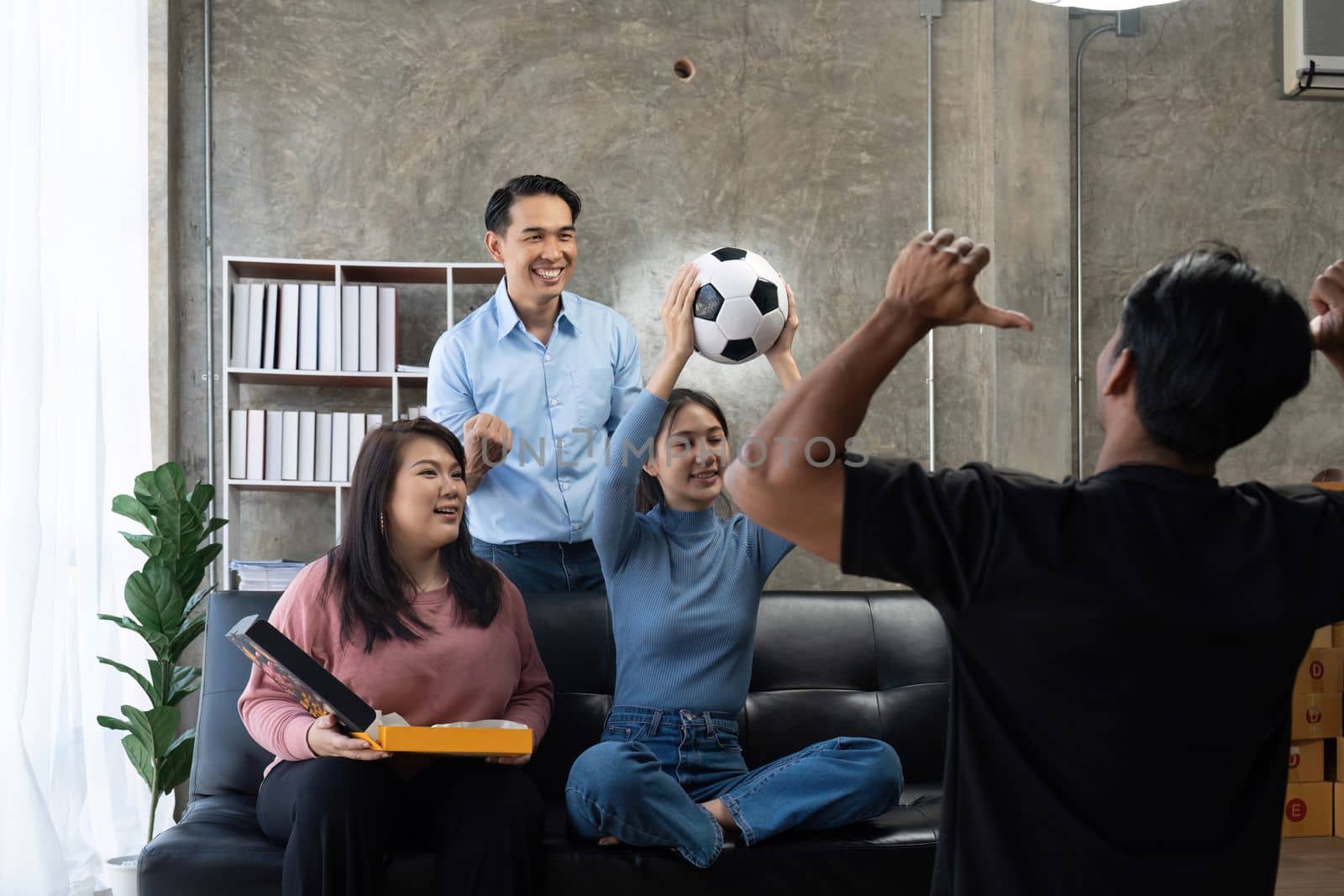 Friends watch sports on TV, cheer and celebrate. Happy diverse asian friend supporters fans sit on couch with popcorn and drinks.