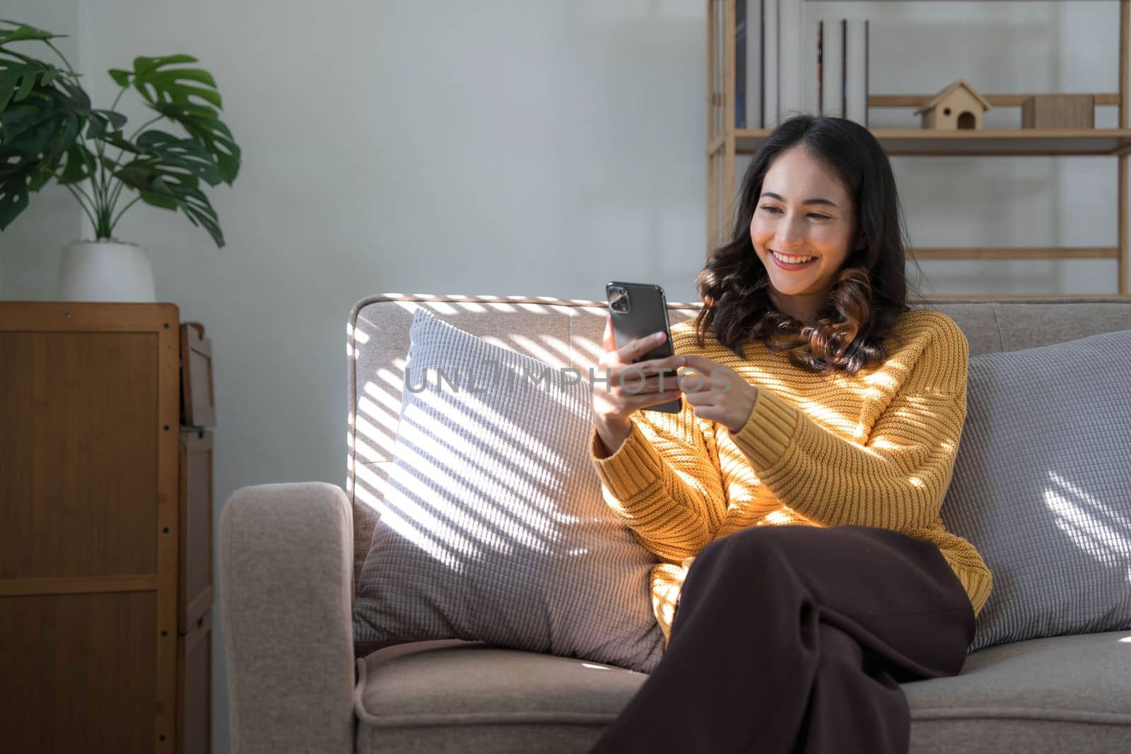 Happy girl checking social media holding smartphone at home. Smiling young latin woman using mobile phone app playing game, shopping online, ordering delivery relax on sofa..