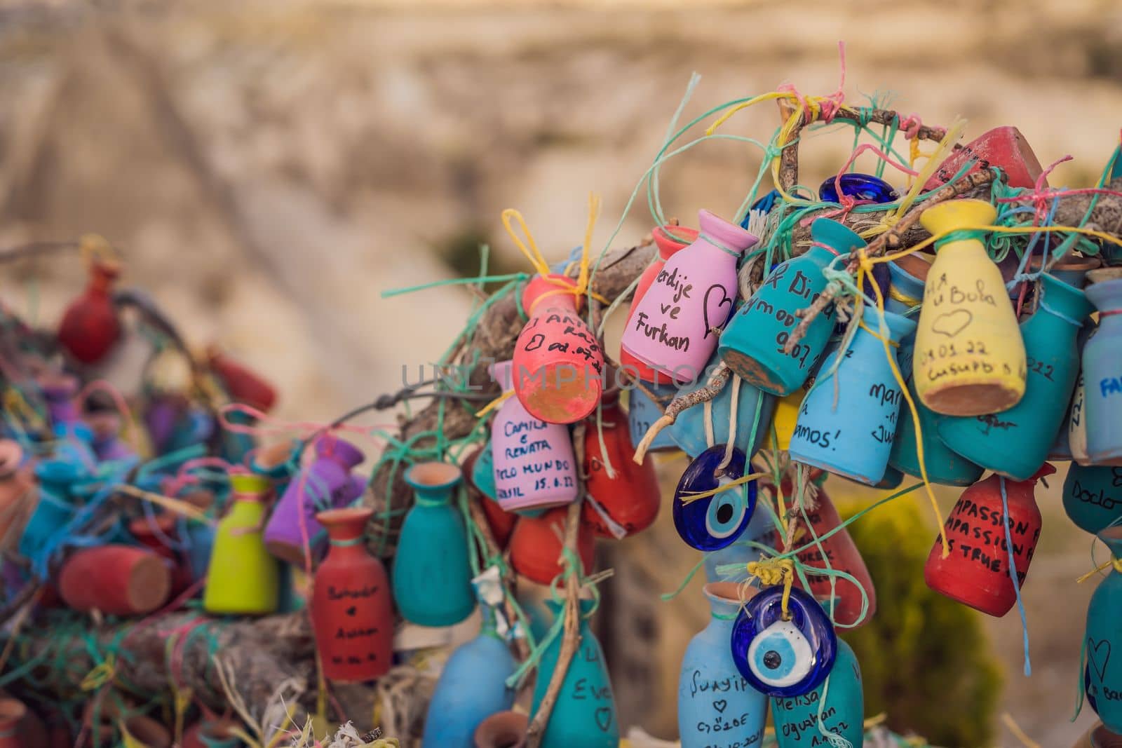 Wish tree. Small multi-colored jugs with inscriptions, wishes hanging on the branches of a tree., against the backdrop of sand ruins and blue sky by galitskaya