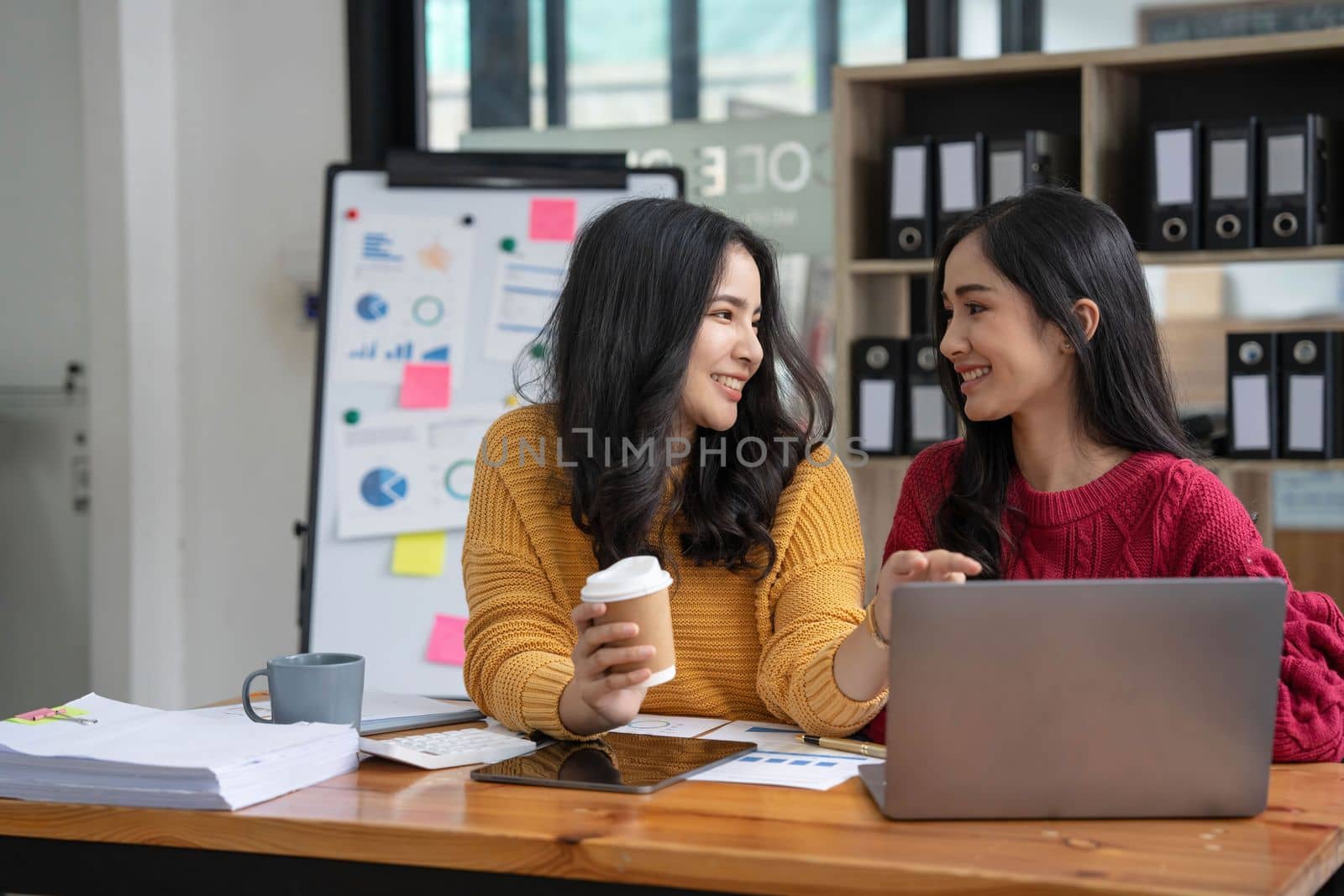 Two young Asian business woman talk, consult, discuss working with new startup project idea presentation analyze plan marketing and investment in the office. by wichayada