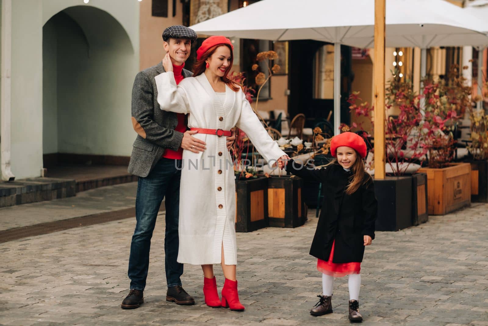 A stylish family of three strolls through the autumn city posing for a photographer . Dad, mom and daughter in the autumn city.