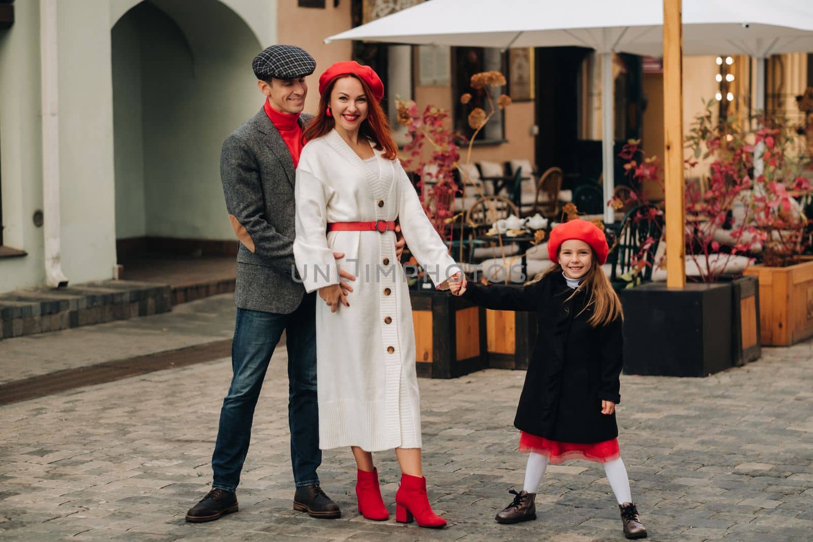 A stylish family of three strolls through the autumn city posing for a photographer . Dad, mom and daughter in the autumn city.