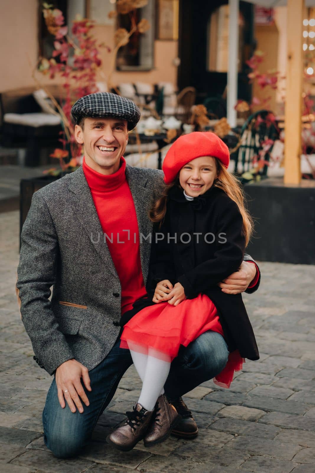 Portrait of a father and daughter sitting on a knee and being on a city street in autumn.