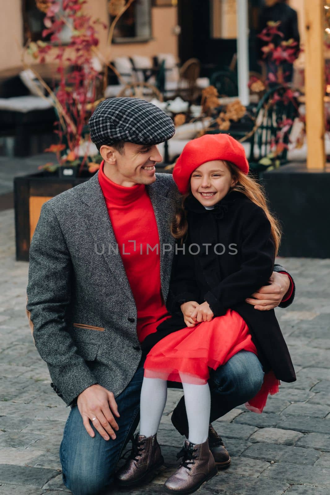 Portrait of a father and daughter sitting on a knee and being on a city street in autumn.