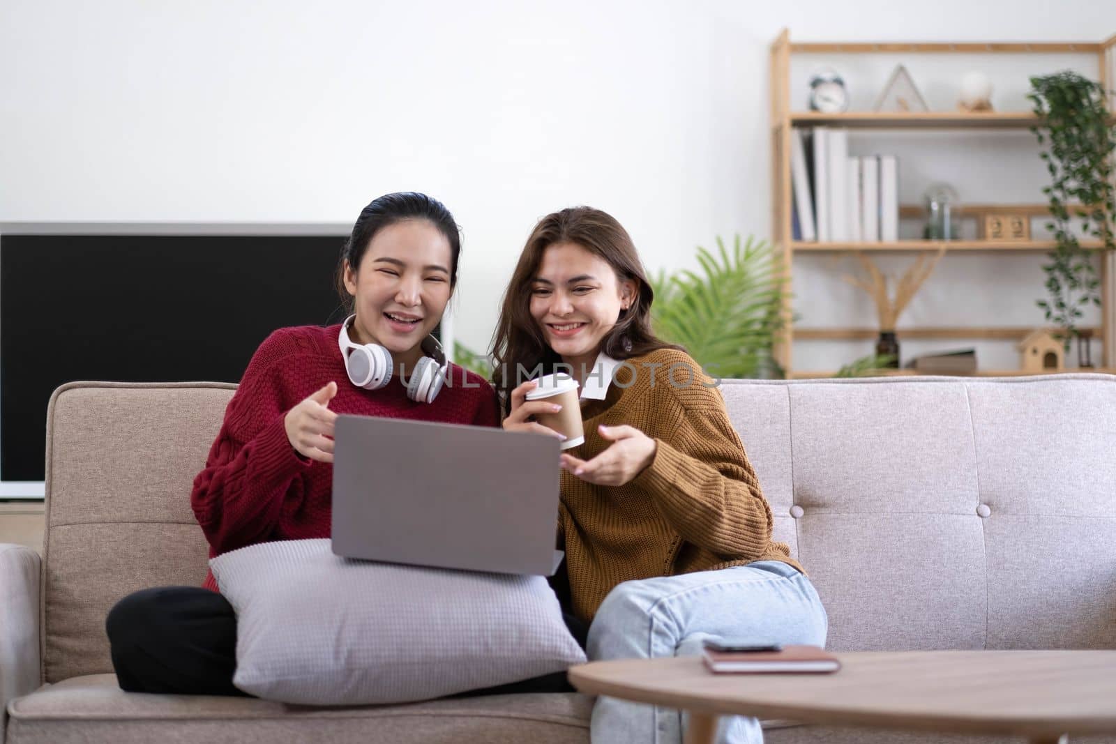 Two asian young woman happy smiling and using computer laptop on couch in living room at home.