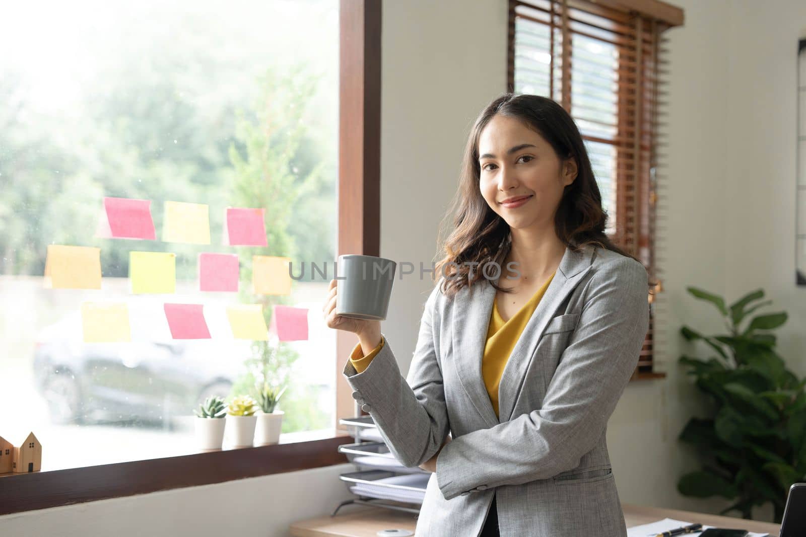 Beautiful young Asian businesswoman smiling holding a coffee mug and laptop working at the office..