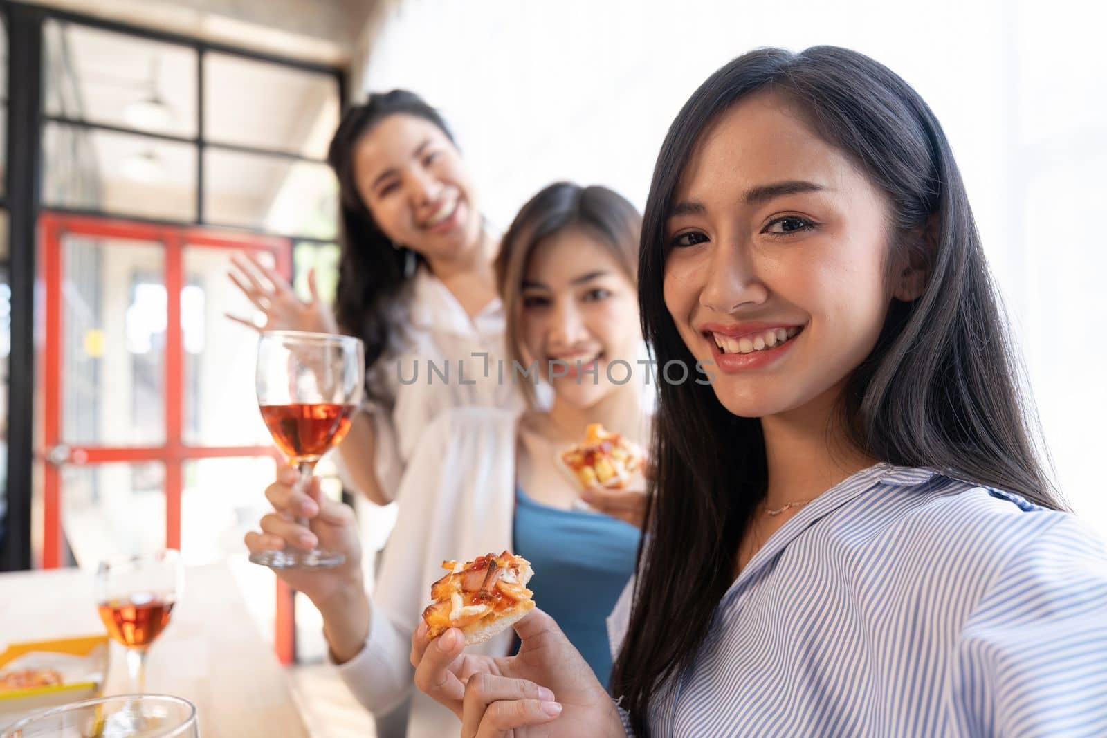 Group of Asian friends gather to celebrate Christmas with champagne and eating pizza at home. Joy of holiday party with friends or colleague concept.