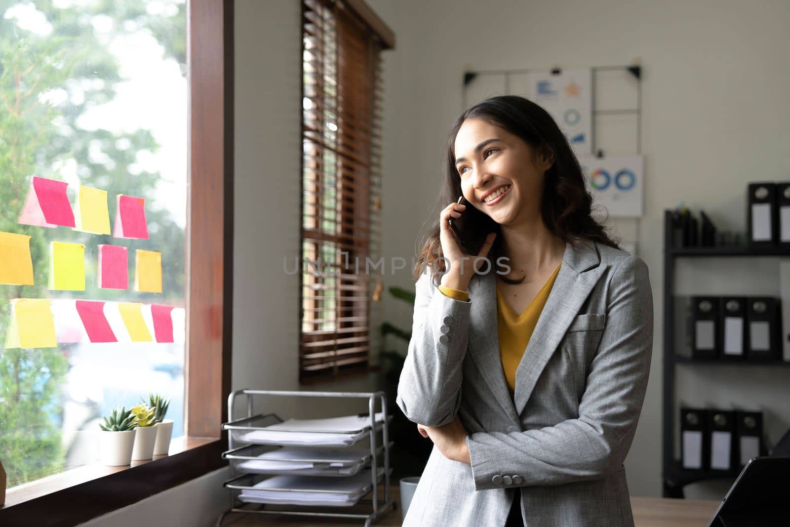 Smiling beautiful Asian businesswoman analyzing chart and graph showing changes on the market and holding smartphone at office..