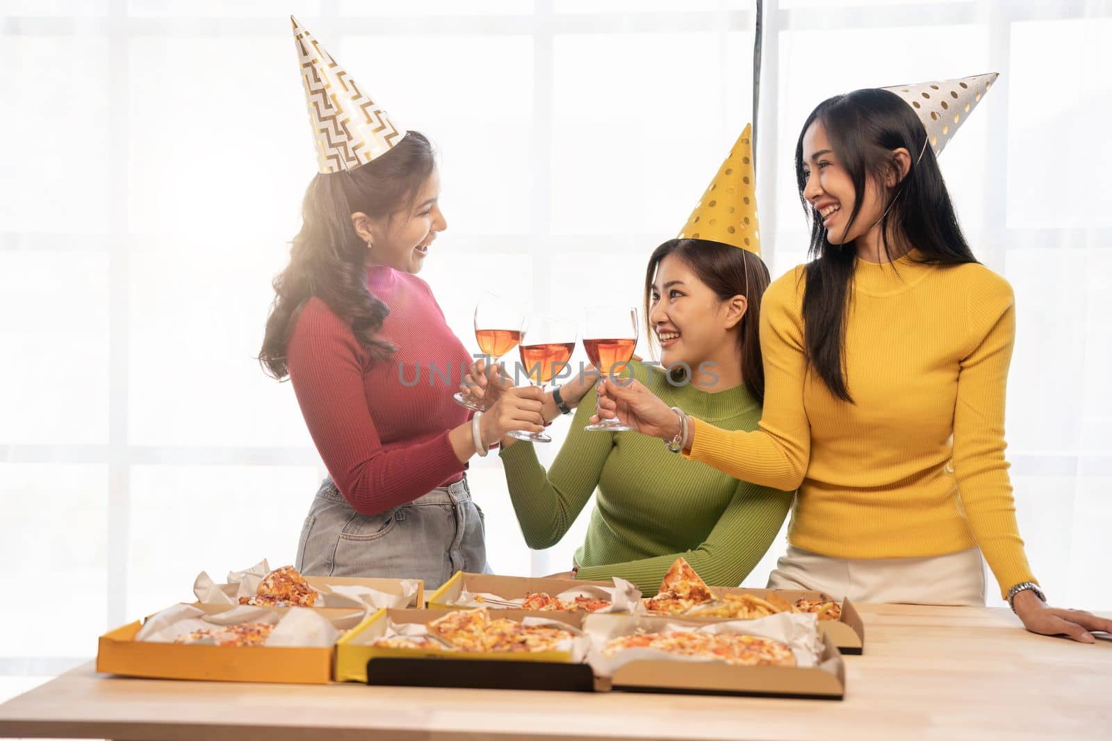 Group of Asian friends gather to celebrate Christmas with champagne and eating pizza at home. Joy of holiday party with friends or colleague concept.