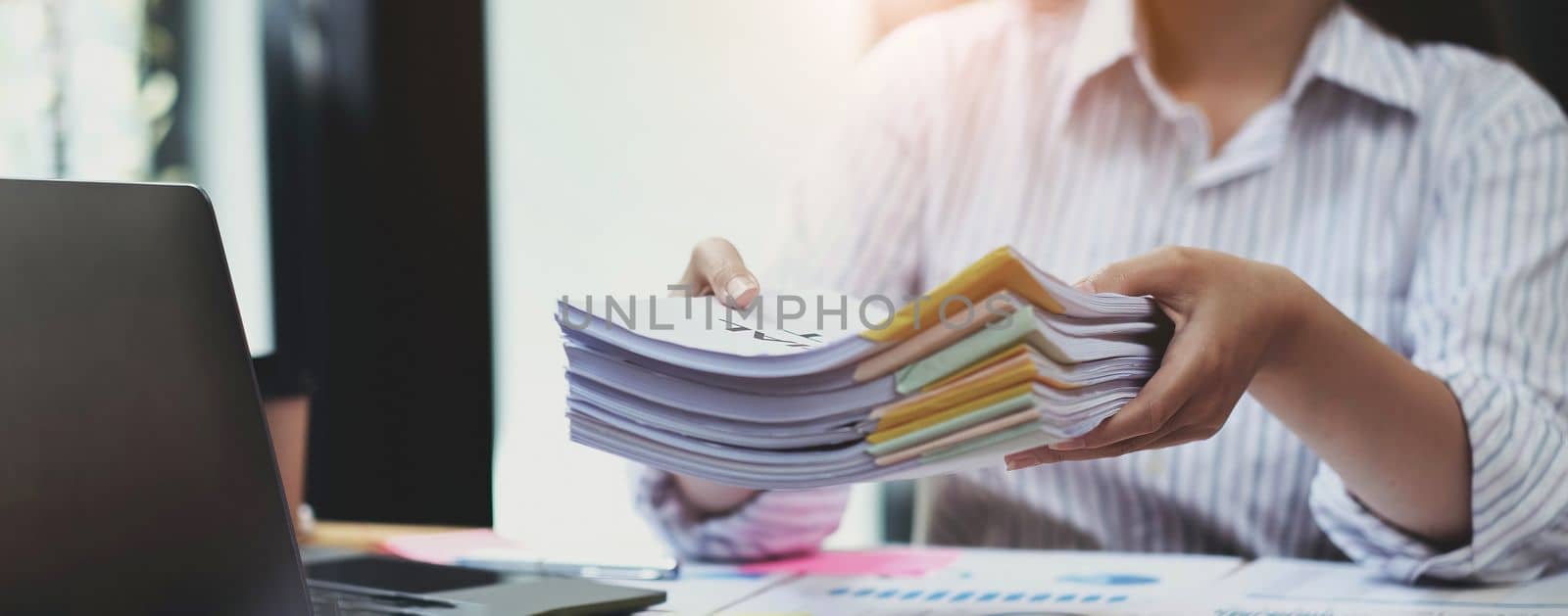 Business Documents concept : Employee woman hands working in Stacks paper files for searching and checking unfinished document achieves on folders papers at busy work desk office. Soft focus.